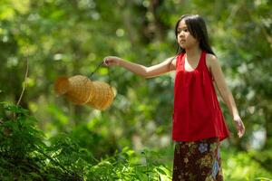 poco asiatico ragazza nel rosso vestito Tenere pesca attrezzatura nel il foresta, rurale Tailandia vivente vita concetto foto