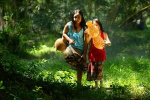 Due ragazze asiatico donne con tradizionale capi di abbigliamento In piedi nel il foresta pluviale. essi aveva divertimento giocando insieme prima assistere Nonno nel attraente pesce nel un' nelle vicinanze lago. foto