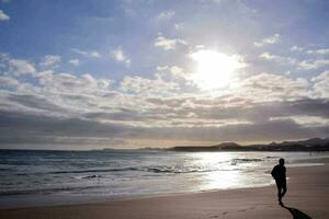 un' persona a piedi su il spiaggia nel davanti di il sole foto