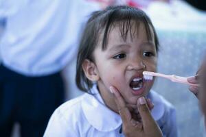 un' cura madre delicatamente spazzole sua poco di figlia denti per bene dentale Salute. foto