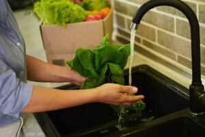 avvicinamento donna mani lavaggio verdure e verdura nel il cucina a casa, preparazione salutare insalata per cena. foto