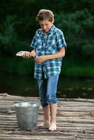 un' pescatore ragazzo ammira il suo presa. pesca bambino. foto