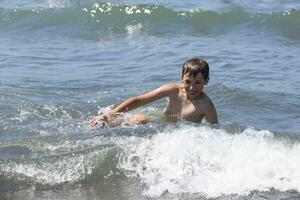 contento ragazzo nuotate nel il mare, giochi con il onde. bambino su vacanza a il mare. foto