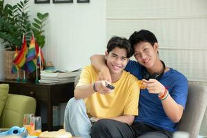 ritratto di Due giovane asiatico gay coppie seduta su divano, la spesa loro gratuito tempo e Guardando tv a casa insieme, concetto per stile di vita di lgbt persone in giro il mondo. foto