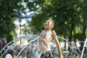 un' poco ragazzo gode il freddo acque di un' Fontana durante il calore onda. concettuale fotografia di caldo tempo atmosferico, calore onda, globale riscaldamento, estate stagione, clima modificare, godere vita. foto