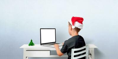 ragazzo nel Natale cappello lavori su il computer portatile con isolato schermo. modello per saluto testo od app, ragnatela pagina presentazione.. copia spazio per vacanza creatività foto