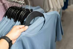 vicino su di uomo mano la scelta un' sconto camicia Abiti nel negozio, ricerca o acquisto a buon mercato cotone camicia su cremagliera appendiabiti a Pulce mercato. uomo la scelta Abiti a negozio. foto