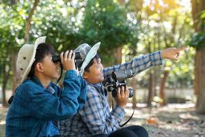 asiatico ragazzi uso binocolo per Guarda a uccelli nel un' Comunità foresta possedere. il concetto di apprendimento a partire dal apprendimento fonti al di fuori il scuola. messa a fuoco su il primo bambino. foto