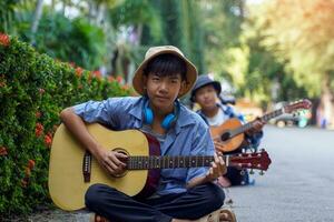 Due asiatico ragazzi erano avendo divertimento giocando classico chitarra insieme durante loro gratuito tempo a un' scuola estate campo a il parco. morbido e selettivo messa a fuoco. foto