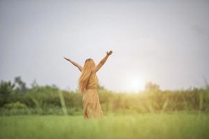 giovane donna in piedi nel campo di erba alzando le mani in aria. foto