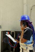 africano americano specialista chiede manager per consigli al di sopra di il Telefono di aria condizionatore bisognoso per essere servito. apprendista controllo Manutenzione Piano dopo finitura interno parti pulizia foto