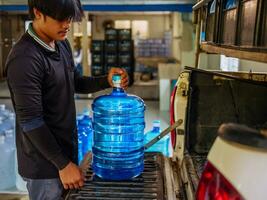 lavoratori sollevamento potabile acqua chiaro e pulito nel blu plastica gallone in il indietro di un' trasporto camion purificato potabile acqua dentro il produzione linea per preparare per vendita.piccolo attività commerciale foto