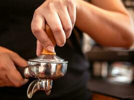 mano di un' barista Tenere un' portafilter e un' caffè manomettere fabbricazione un caffè espresso caffè. barista presse terra caffè utilizzando un' manomettere nel un' caffè negozio foto