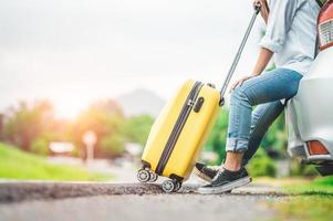 primo piano parte inferiore del corpo della donna che si rilassa sul bagagliaio dell'auto con i bagagli del carrello foto