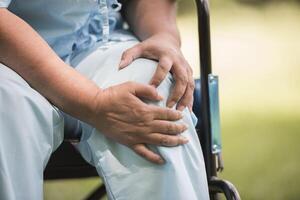 donna anziana seduta su sedia a rotelle con dolore al ginocchio foto