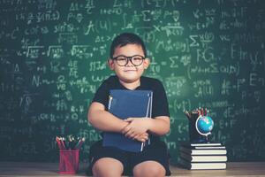 ragazzo con libri seduto vicino alla lavagna verde foto