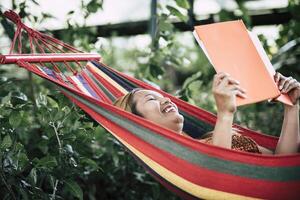 giovane donna che legge un libro sdraiata su un'amaca foto