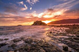 un' tramonto al di sopra di il oceano con rocce e un' piccolo isola foto