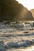 un' onda è rottura su il spiaggia con roccia nel il sfondo foto