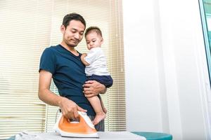 papà single sta stirando mentre trasporta suo figlio. persone e stili di vita foto