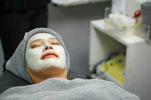 avvicinamento bellezza donna con bianca maschera crema su sua viso nel bellezza clinica. foto