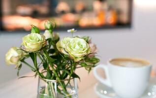 bellissimo Rose nel un' vaso e un' tazza di cappuccino su un' tavolo nel un' bar. avvicinamento. selettivo messa a fuoco. foto