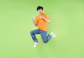 uomo asiatico che salta e tiene in mano uno smartphone, isolato su verde foto