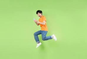 uomo asiatico che salta e tiene in mano uno smartphone, isolato su verde foto