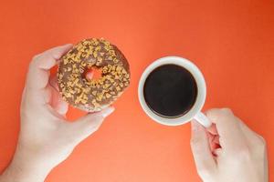 le mani maschili tengono una tazza di caffè americano caldo e una ciambella al cioccolato foto