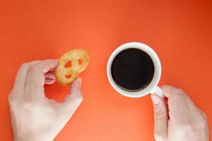 le mani maschili tengono una tazza di caffè americano caldo e biscotti su un luminoso foto