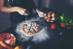 donne asiatiche che preparano una pizza, sul tavolo della cucina foto