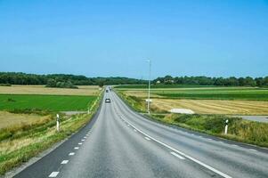 un' lungo vuoto strada con un' blu cielo e verde i campi foto