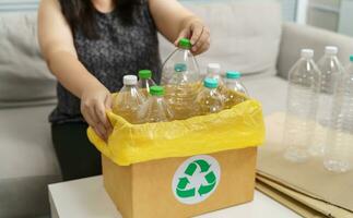 casa riciclare eco verde zero concetto donna lancio vuoto plastica bottiglia nel raccolta differenziata bidone con giallo spazzatura borse a casa. foto