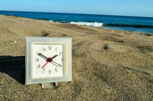 un' orologio su il spiaggia con il oceano nel il sfondo foto