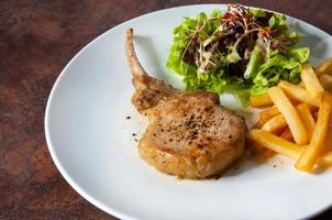 bistecca di braciola di maiale con insalata e patatine fritte foto