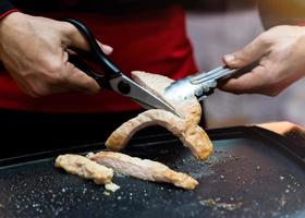 tenere in mano le forbici che tagliano la bistecca di maiale alla griglia foto