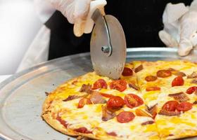 primo piano mano dello chef che taglia la pizza in cucina foto