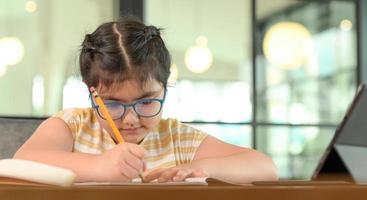 bambina con gli occhiali sta studiando a casa con un'espressione seria. foto