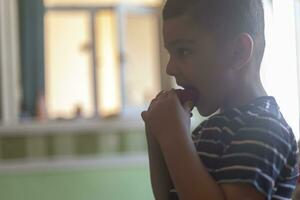un' poco ragazzo mangiare fragole. estate cibo. un' giovane ragazzo mangia un' delizioso fragola nel caldo estate giorno foto