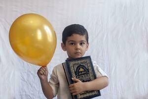 un' giovane mezzo orientale ragazzo con il santo corano. ritratto di 5 anni vecchio musulmano ragazzo Tenere un' santo Corano con bianca sfondo. gratuito spazio foto