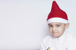 ritratto di un' sei anni ragazzo contro il bianca sfondo. festeggiare Natale. 6-7 anno vecchio ragazzo con Santa cappello. foto