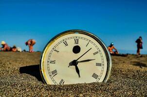 un' orologio su il spiaggia con persone nel il sfondo foto