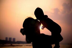 silhouette di madre giochi con sua bambino piccolo contro il tramonto. foto