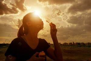 un' Sud est asiatico ragazza è soffiaggio bolle in il aria a tramonto. foto