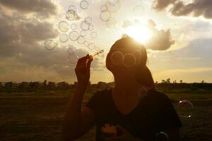 un' Sud est asiatico ragazza è soffiaggio bolle in il aria a tramonto. foto