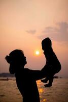 silhouette di madre giochi con sua bambino piccolo contro il tramonto. foto