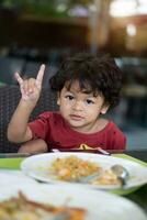 Riccio capelli asiatico bambino mangiare prima colazione nel un' ristorante foto