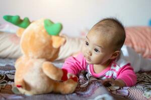 6 mese vecchio asiatico bambino ragazza è sorridente, godendo il suo Bambola. foto