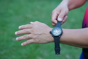 vicino su uomo mano è indossare nero orologio su il suo polso, verde all'aperto sfondo. concetto, alla moda accessorio per tempo raccontando, rendere voi Guarda elegante, puntuale e inteligente. analogico polso guarda. foto