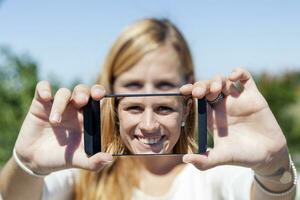 bella donna con biondo capelli prendere un' autoscatto con inteligente Telefono foto